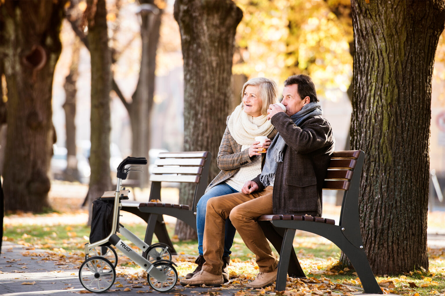 Senior couple sitting on bench, drinking coffee. Sunny autumn nature.